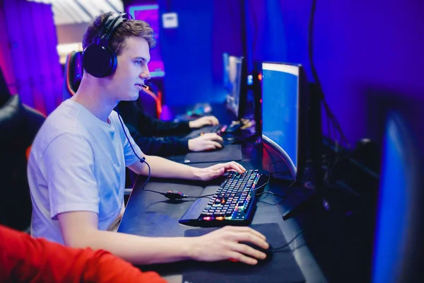 A player in a headset at a keyboard lit in deep blue and purple at a quiet corner station