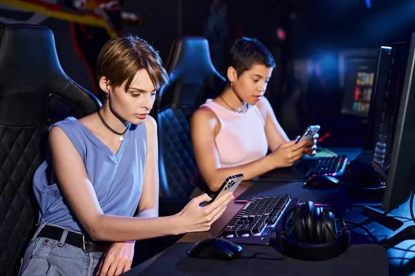 Two players seated side by side at adjacent stations sharing a desk in blue light