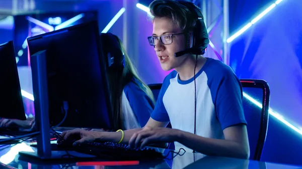 A smiling young player in a headset at a keyboard, lit by orange and blue neon strips